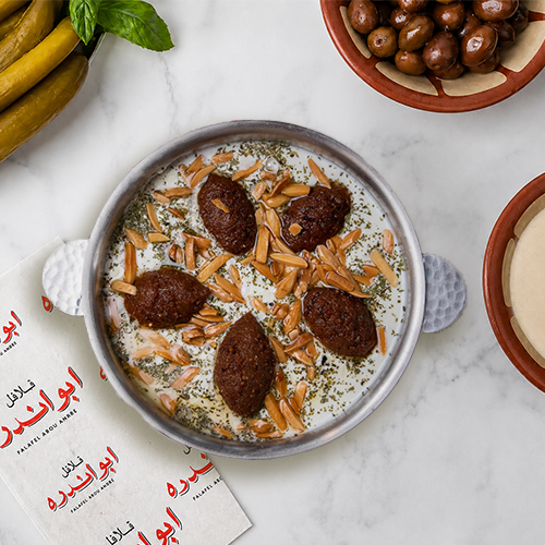 Traditional Fattet Kibbeh from Falafel Abou Andre served in a plate, featuring fresh mint, layer in garlic yogurt sauce, topped with toasted pine nuts,or silvered almonds.