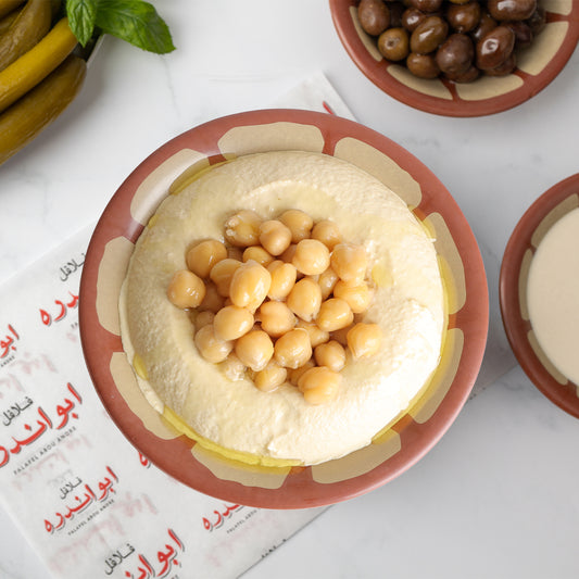 Lebanese Hummus plate at Falafel Abou Andre served with warm chickpeas and tahini, accompanied by tomatoes, radishes, onions, fresh mint, pickled cucumbers and turnips, Lebanese olives, and traditional Lebanese bread.