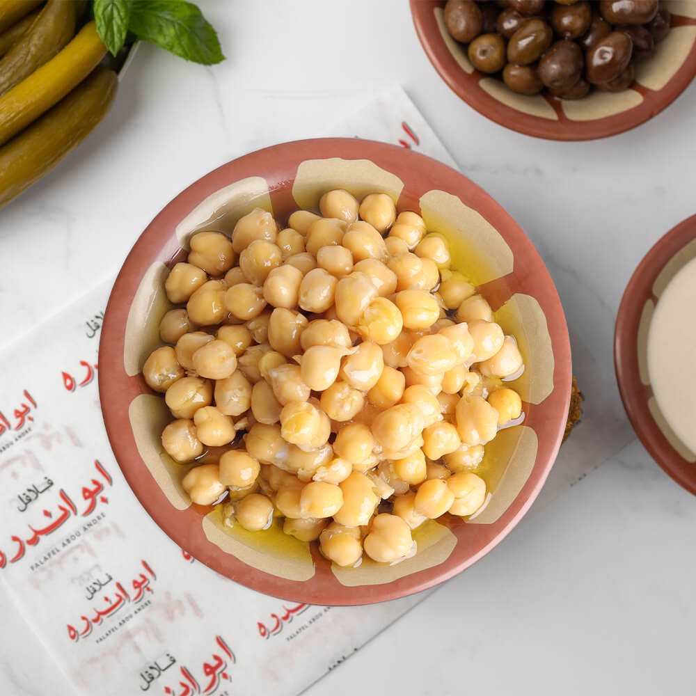 Lebanese Balila plate at Falafel Abou Andre served with warm chickpeas and tahini, accompanied by tomatoes, radishes, onions, fresh mint, pickled cucumbers and turnips, Lebanese olives, and traditional Lebanese bread.