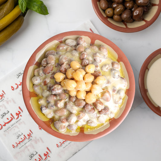 Lebanese Foul with Tahini plate at Falafel Abou Andre served with seasoned fava beans and tahini, accompanied by tomatoes, radishes, onions, fresh mint, pickled cucumbers and turnips, Lebanese olives, and traditional Lebanese bread.