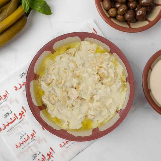 Lebanese Msabaha plate at Falafel Abou Andre served with creamy chickpeas and tahini, topped with tomatoes, radishes, onions, fresh mint, pickled cucumbers and turnips, Lebanese olives, and traditional bread.