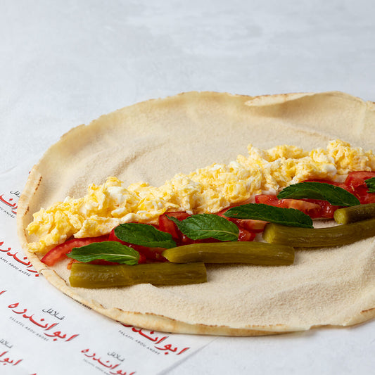 A freshly prepared scrambled large egg sandwich made with soft fluffy scrambled eggs inside toasted bread, fresh mint, tomatoes, and pickles ideal for a hearty breakfast or brunch. A simple and satisfying meal rich in protein, commonly served warm and fresh for a quick nutritious bite.